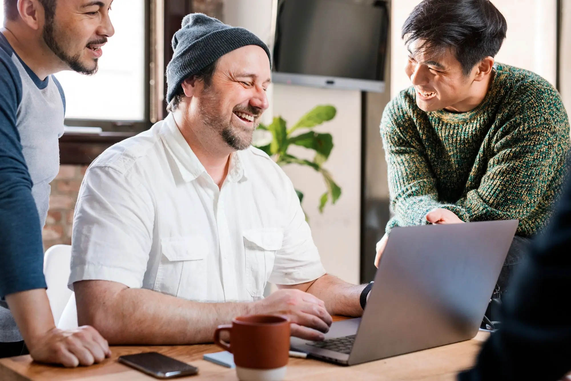 Three people on an agile team gathered around computer laughing